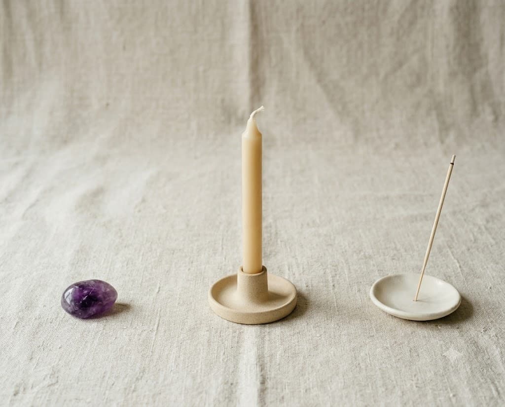 A sparse arrangement of a candle, incense and a single stone on bone linen